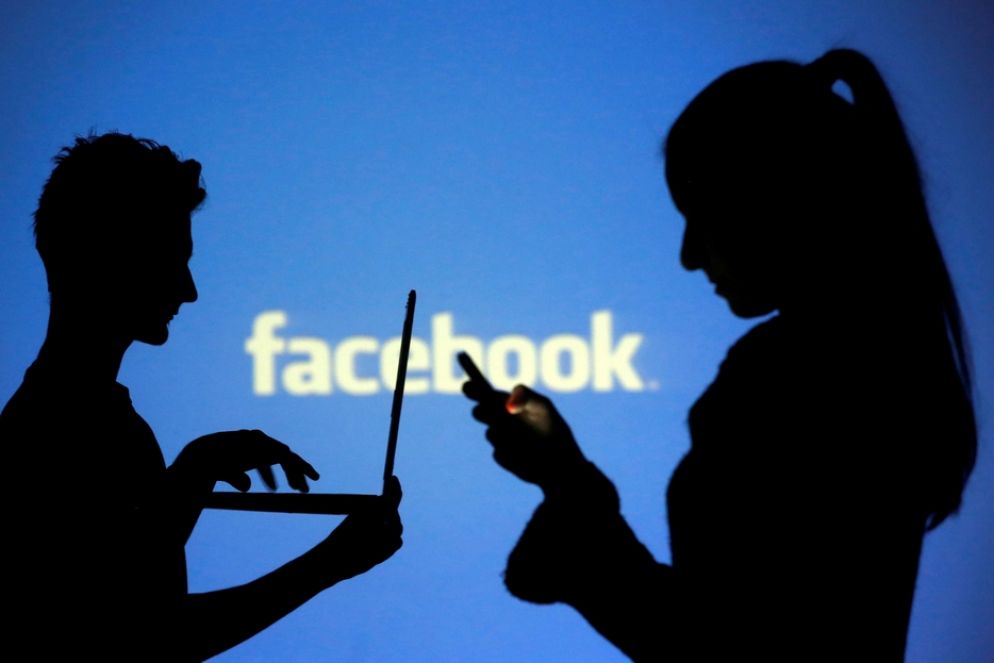 Le ombre di due utenti davanti a un'insegna di Facebook - Reuters